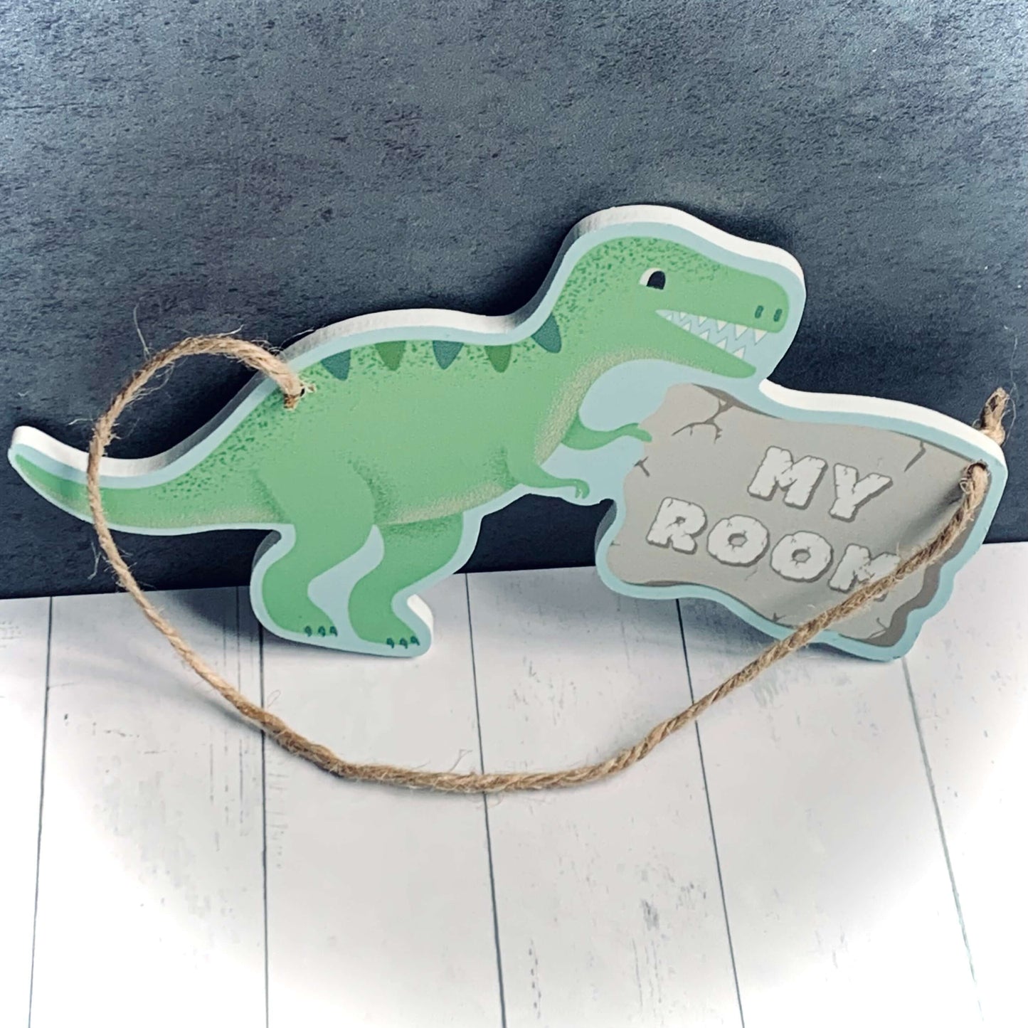 Dinosaur shaped door hanger, with green dinosaur holding a sign saying 'My Room' hung by natural jute string.
From Wickerhearts gift collection.