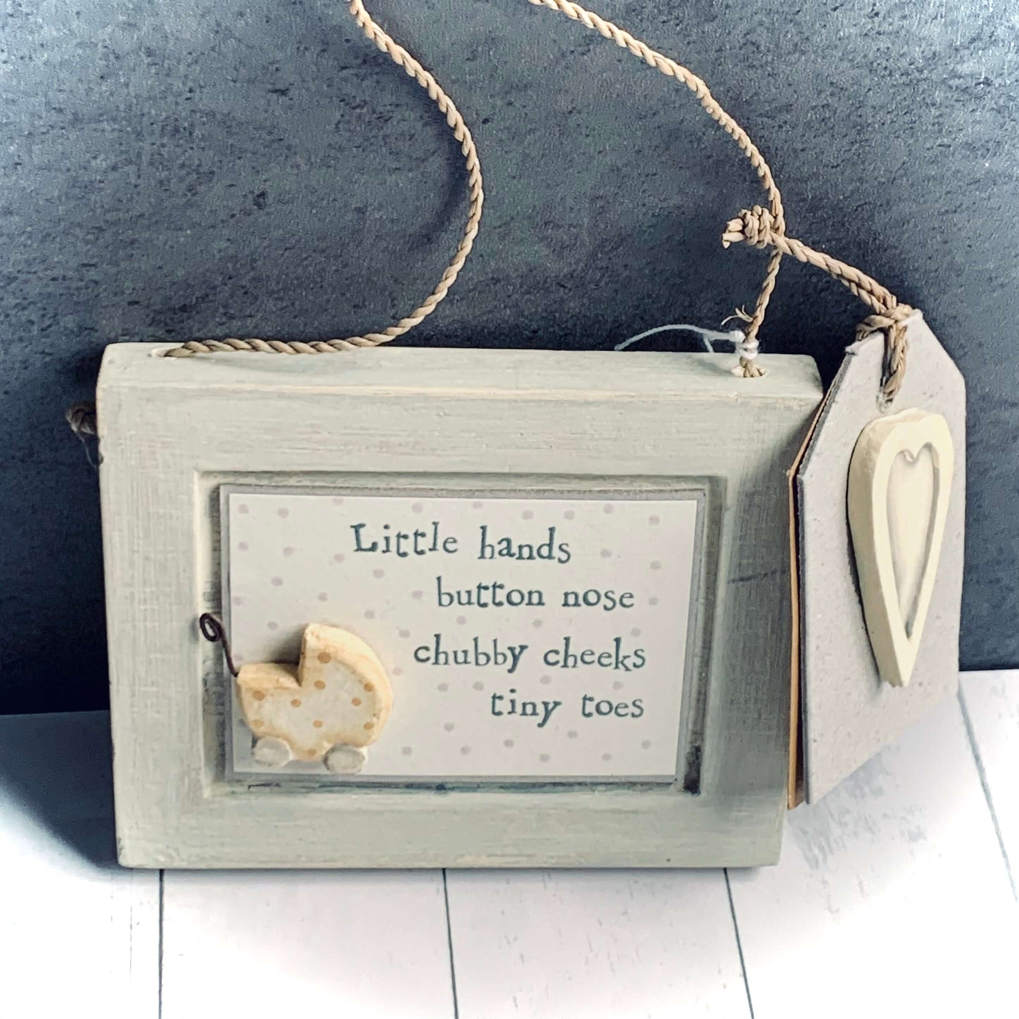 Gorgeous little grey wooden framed picture to hang in baby's nursery.
Wording is 'Little hands button nose chubby cheeks tiny toes' Little wooden pram in lower left corner.
Made by East Of India.
From Wickerhearts gift and East of India collection.