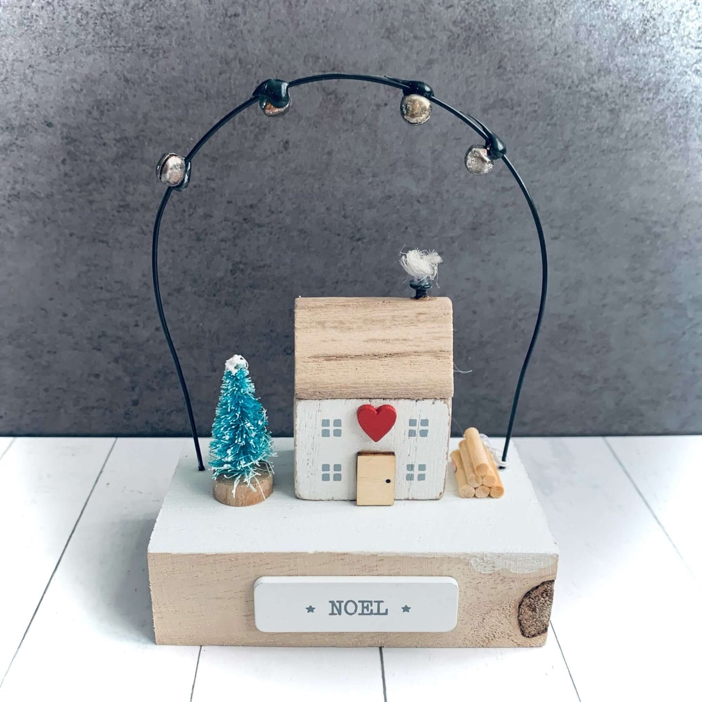Small wooden house with heart on wooden block, wire above with small bells on. The word 'Noel' on front of block. From Wickerhearts Christmas gift collection.