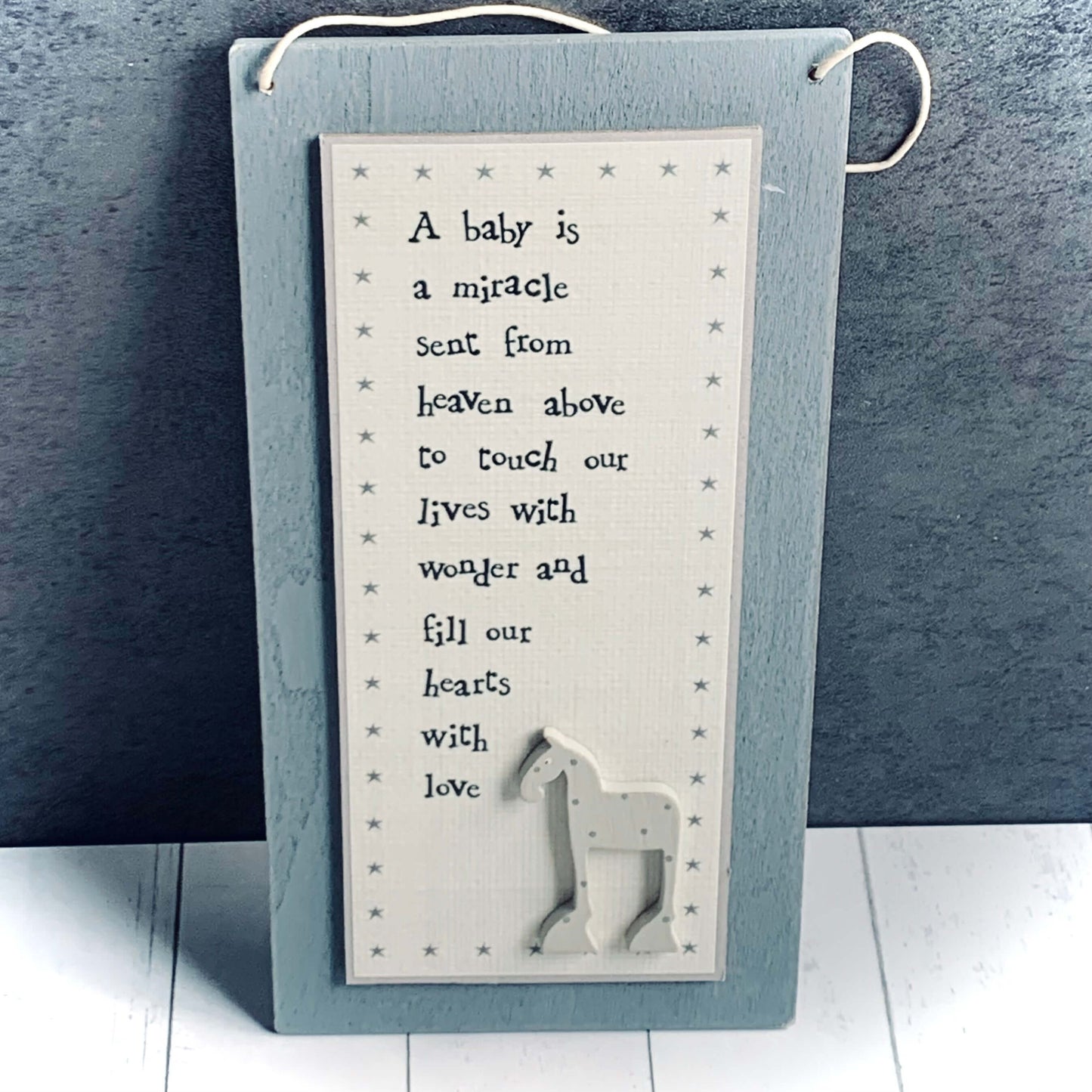 Tall grey, light wood hanging picture with rhyme and small horse at bottom. Words are 'A baby is a miracle sent from heaven above to touch our lives with wonder and fill our hearts with love'. From Wickerhearts East of India gift collection.