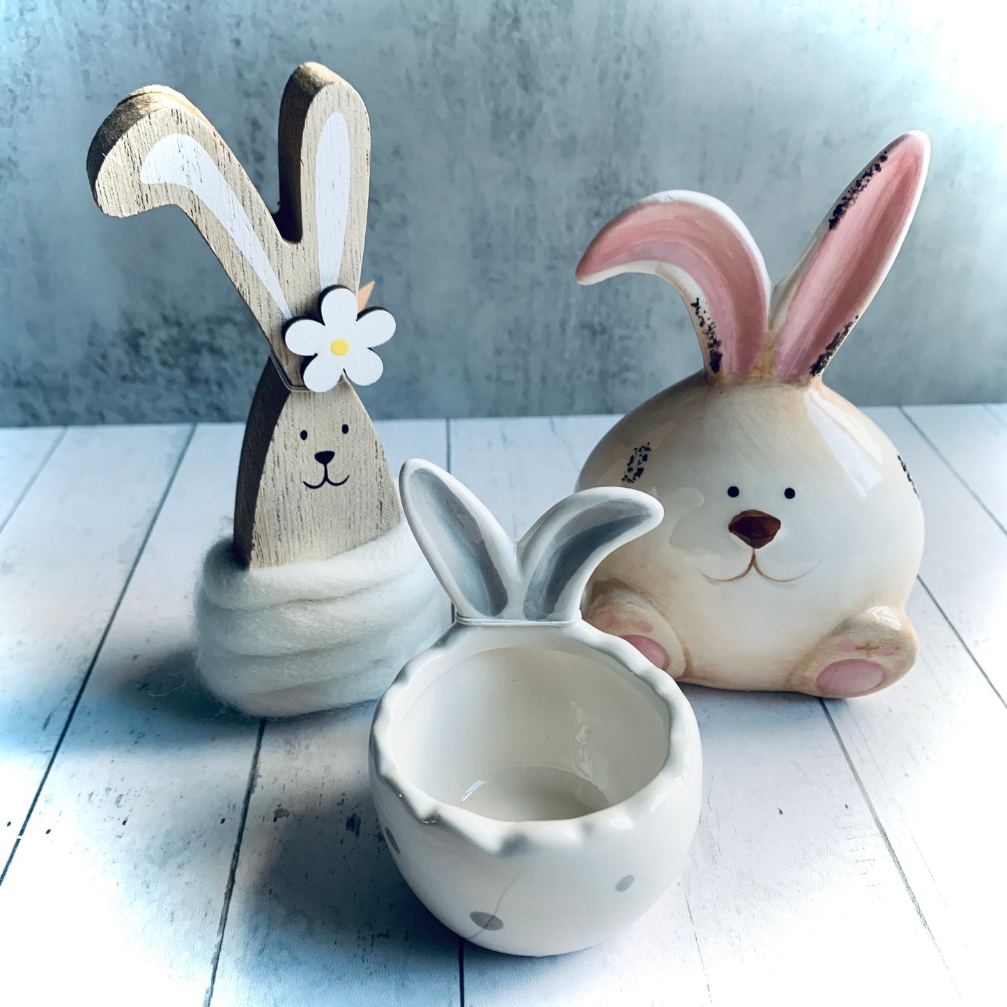 Daisy the chunky wooden bunny decoration alongside a ceramic pink and neutral coloured bunny, with a grey and white spotted egg cup with bunny ears. From Wickerhearts Spring gift and decor collection.