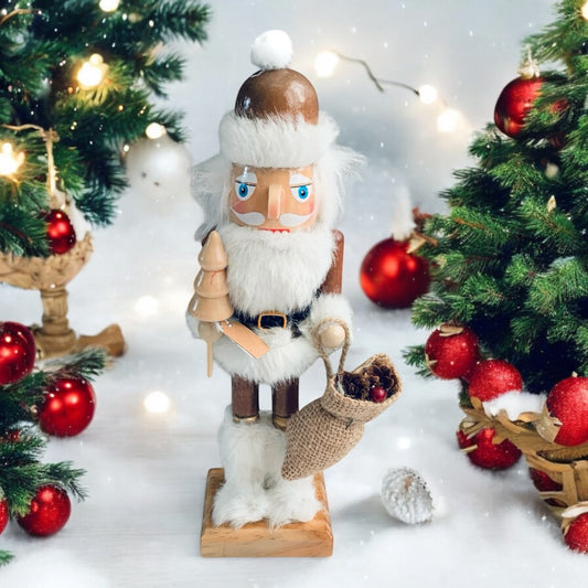 Image of Nordic Santa Nutcracker decoraton, with white beard and hair and white furry boots carrying a small wooden tree and a bag of goodies. From Wickerhearts Christmas gift collection.