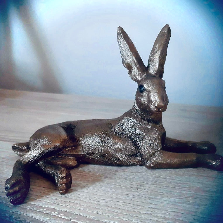 Image of bronze hare lying down on pale wooden counter top. From Wickerhearts gift collection.