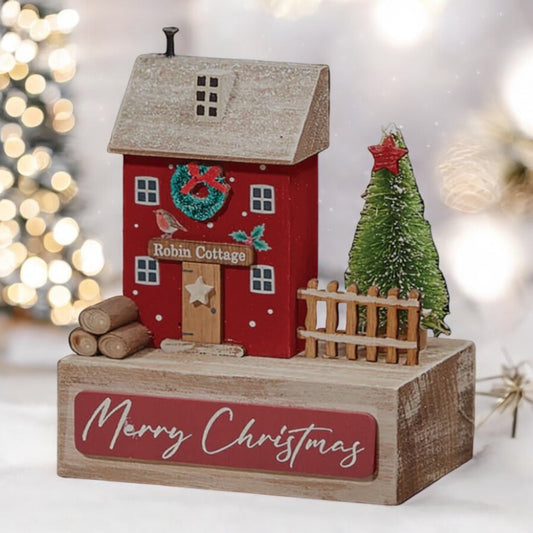 Festive red wooden Robin Cottage on a wooden block with Christmas tree and logs. From Wickerhearts Christmas gift collection.