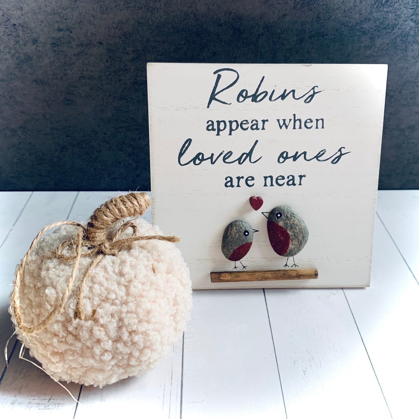 Square, white wooden small picture of 2 pebble robins on a branch with a love heart. The wording is 'Robins appear when loved ones are near'. This item is a bestseller from Wickerhearts Christmas and gift collection. Next to it is a neutral coloured small pumpkin for decoation.