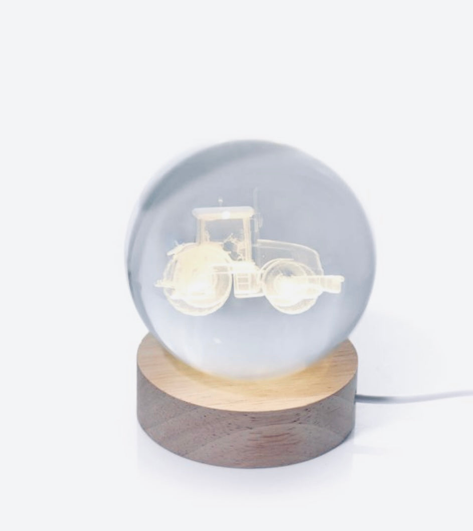 Glass sphere with tractor silhouette on a wooden base against a white background