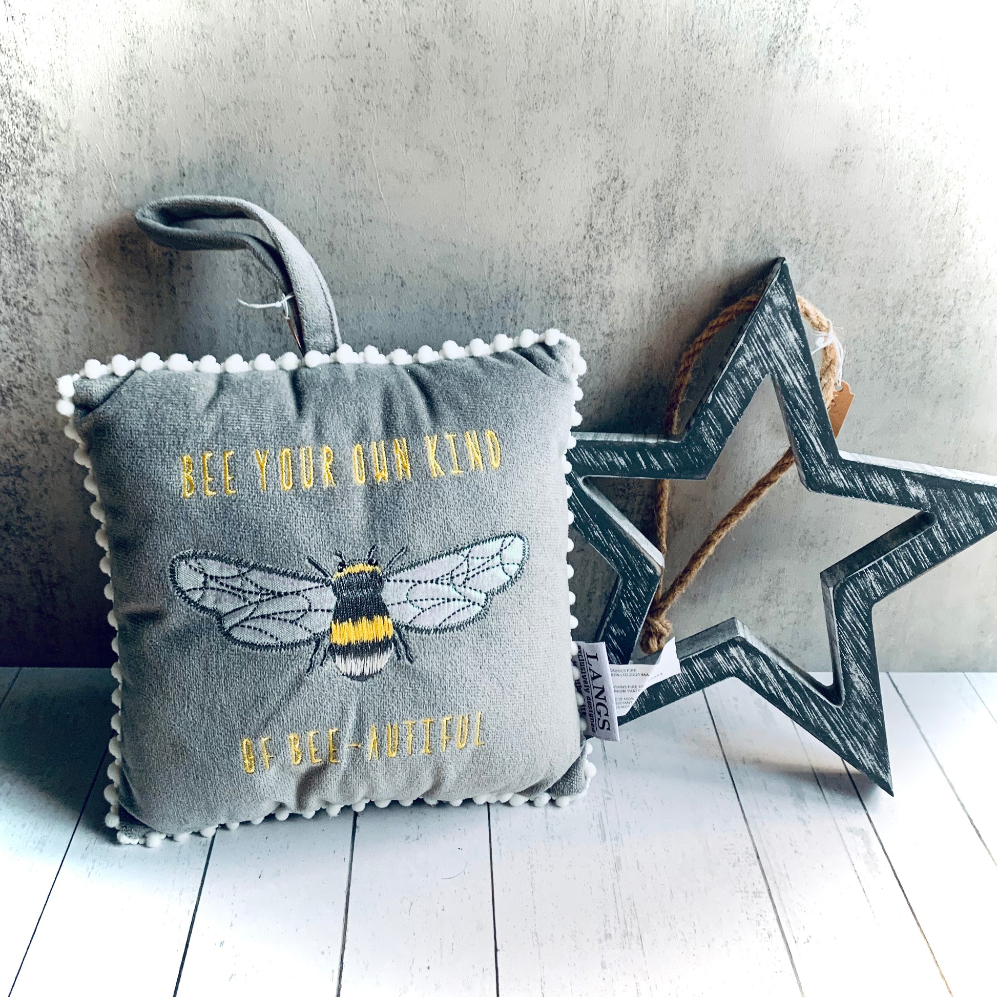 Mini grey velvet cushion with a bee embroidered on the front and the words 'Bee your own kind of Bee-autiful'. Pictured styled next to a rustic grey star. From the Spring 2024 gift collection at Wickerhearts.