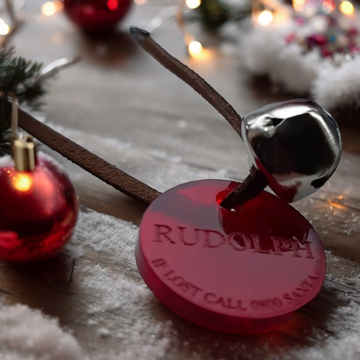 Close up image of Rudolf's Tag. Red round tag with wording 'Rudolf - If lost call 0800Santa. Tag is on small piece of dark leather with silver bell attached. Part of Christmas Eve Surprise bundle for Children From Wickerhearts Christmas gift collection.