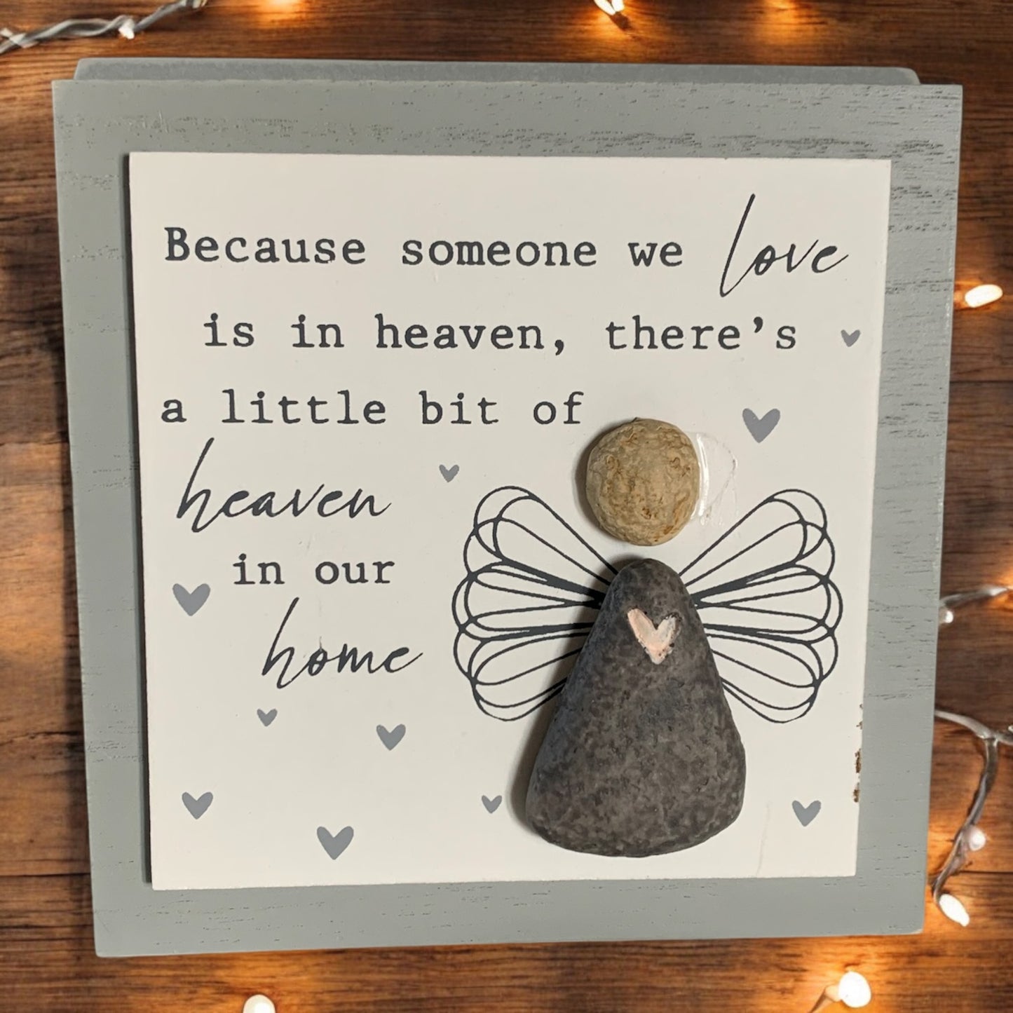 Front image of grey and white wooden memorial picture, featuring pebble angel with the words 'Because someone we love is in heaven, there's a little bit of heaven in our home.' From the Autumn and Christmas gift collection at Wickerhearts.