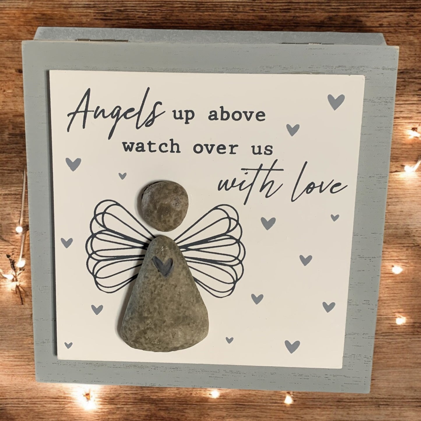 Front image of grey and white wooden memorial picture, featuring a pebble angel with the words 'Angels up above watch over us with love.' From the Autumn and Christmas gift collection at Wickerhearts.